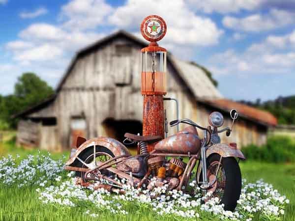 A rusted vintage motorcycle propped up against a vintage gas pump in the middle of the green meadow. An old barn in the background.