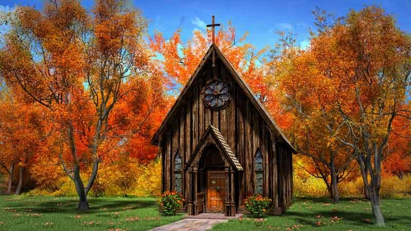 A Littlle brown wooden church set in a beautiful green grass yard.  An absolutely gorgeous thick Autumn forest in the background
